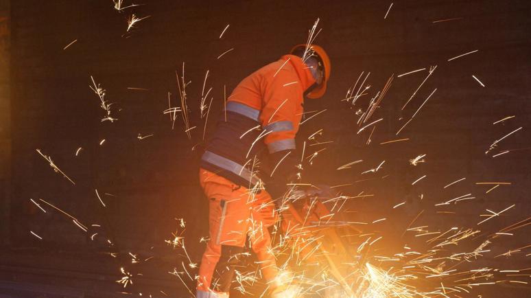 Ein SBB-Mitarbeiter in oranger Arbeitskleidung am schweissen